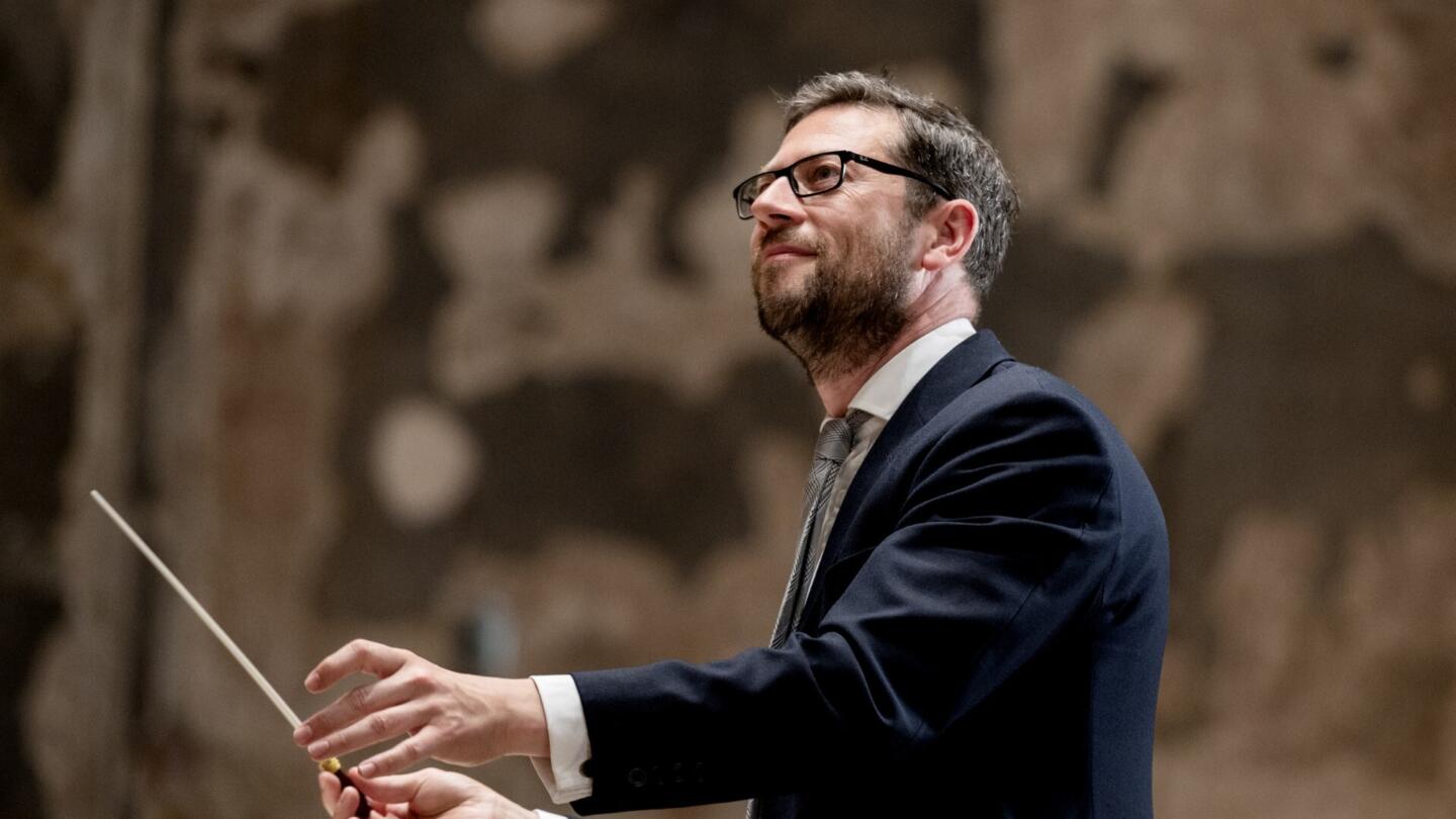 John Wilson standing holding a baton to conduct